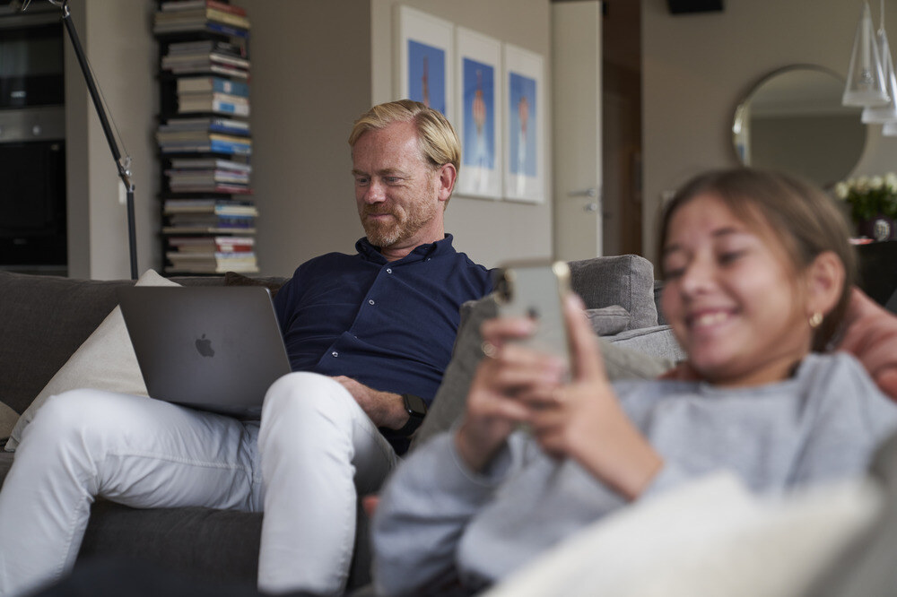 mand og datter sidder i sofa med telefon og computer